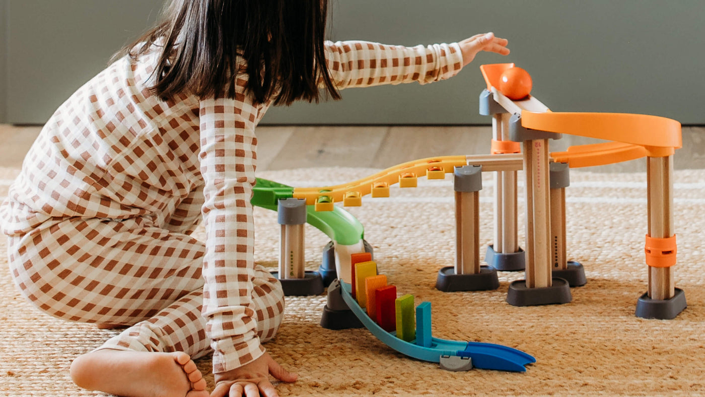 Child playing with a colorful marble run toy on a carpet.