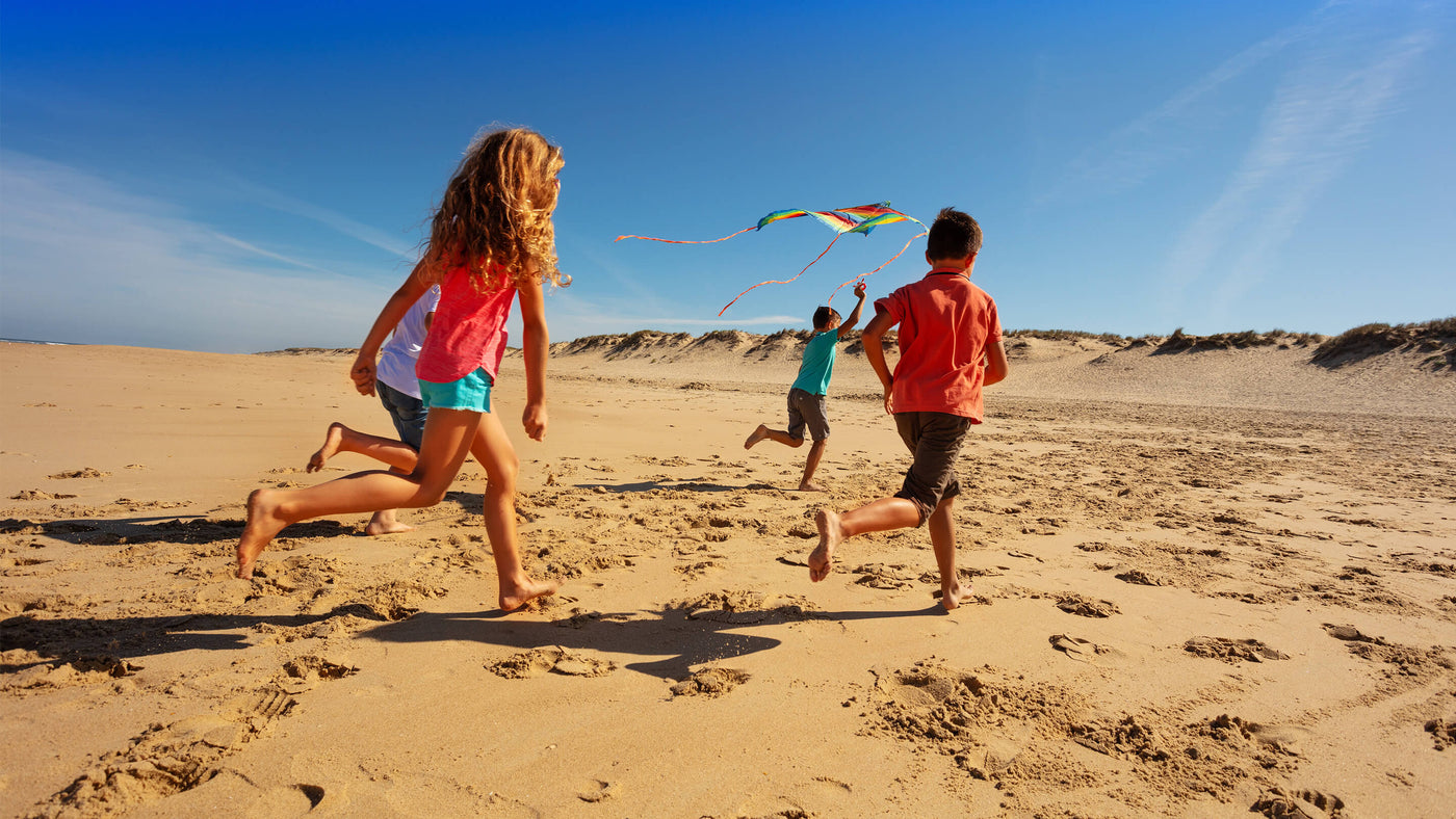 Group of kids run away with a kite on a beach