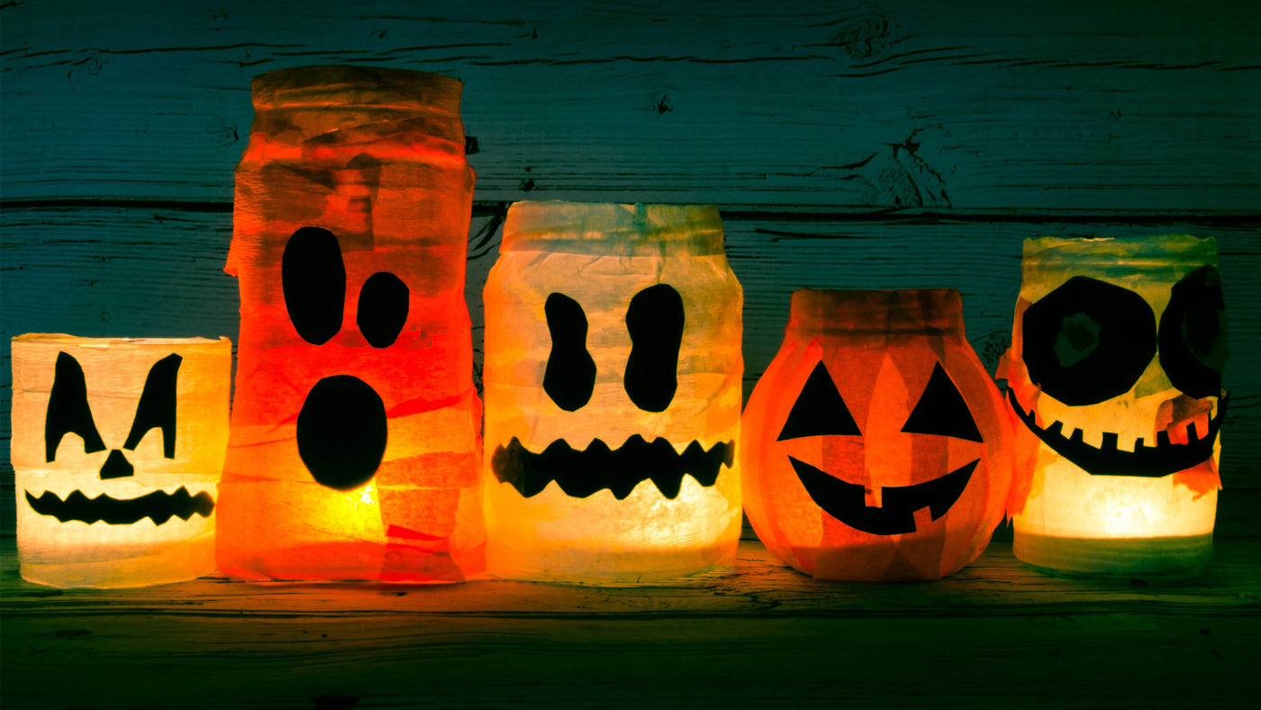 A row of glowing Halloween lanterns with various spooky faces, including a pumpkin, ghost, and skull designs, set against a wooden background.