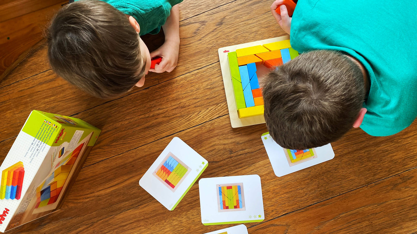 Overhead view of 2 boys looking down on a colorful board of wooden shapes with template cards