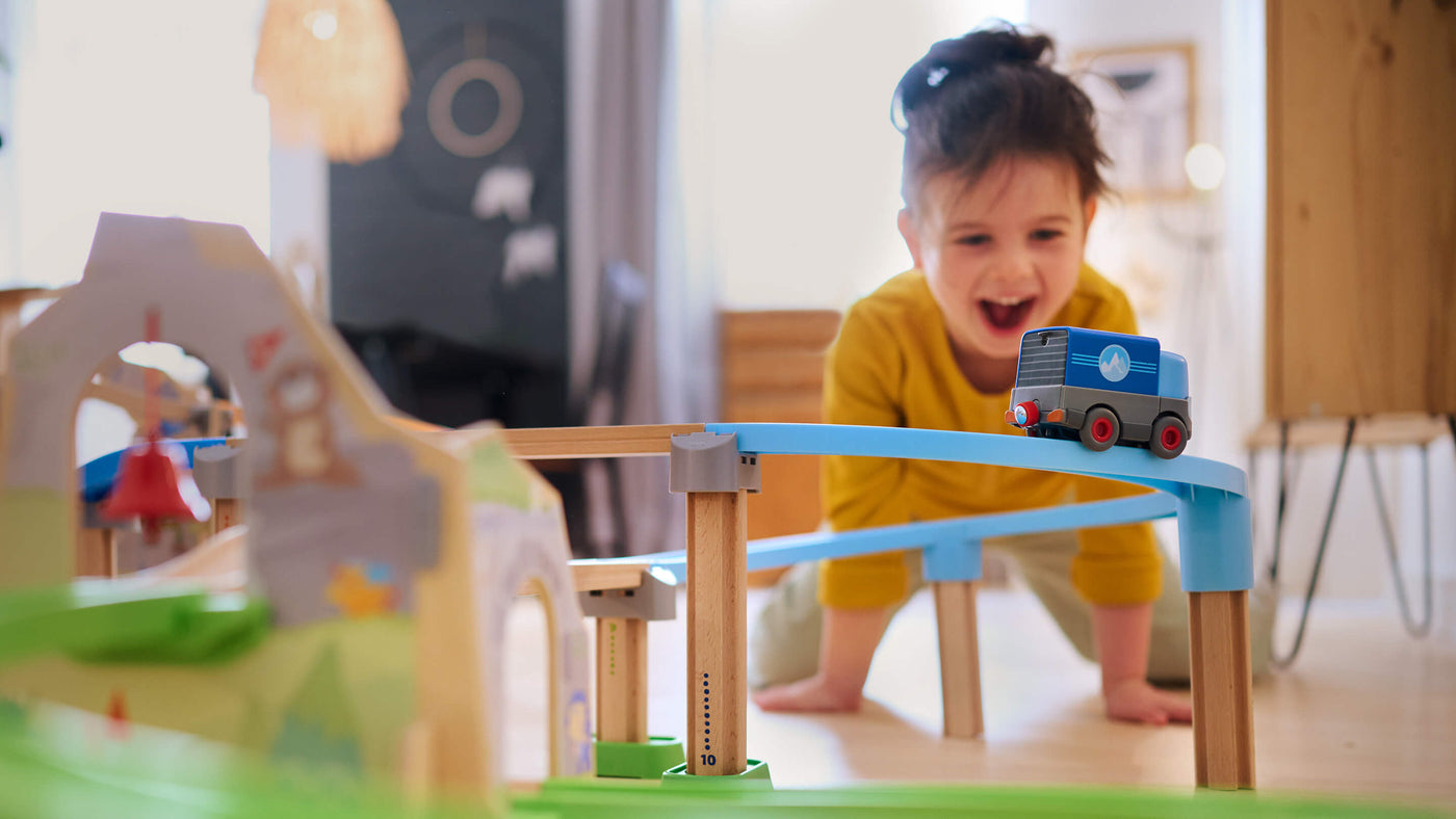 Laughing girl looking at a toy truck traveling down an elevated, curved Kullerbü track