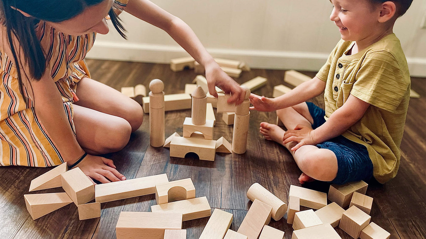 Two children playing with wooden building blocks on the floor.