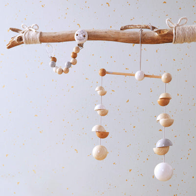 A wooden branch hangs with HABA Wooden Dots Mobile made of spherical wooden beads in neutral tones, set against a softly textured background.