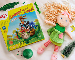 A colorful game box titled "Animal Upon Animal" beside a smiling Mali doll, green decorations, and a small Christmas tree.