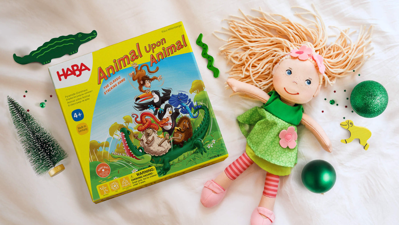 A colorful game box titled "Animal Upon Animal" beside a smiling Mali doll, green decorations, and a small Christmas tree.