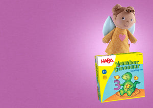 Plush angel doll with a yellow dress and a HABA game box titled "Number Dinosaur" on a purple background.