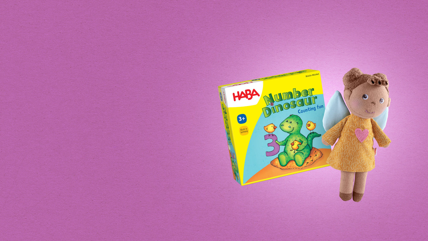 Plush angel doll with a yellow dress and a HABA game box titled "Number Dinosaur" on a purple background.