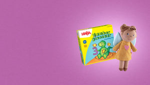 Plush angel doll with a yellow dress and a HABA game box titled "Number Dinosaur" on a purple background.