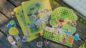 Orchard themed wooden threading game, wooden pieces, templates and a glass of orange juice sitting on a picnic table outside