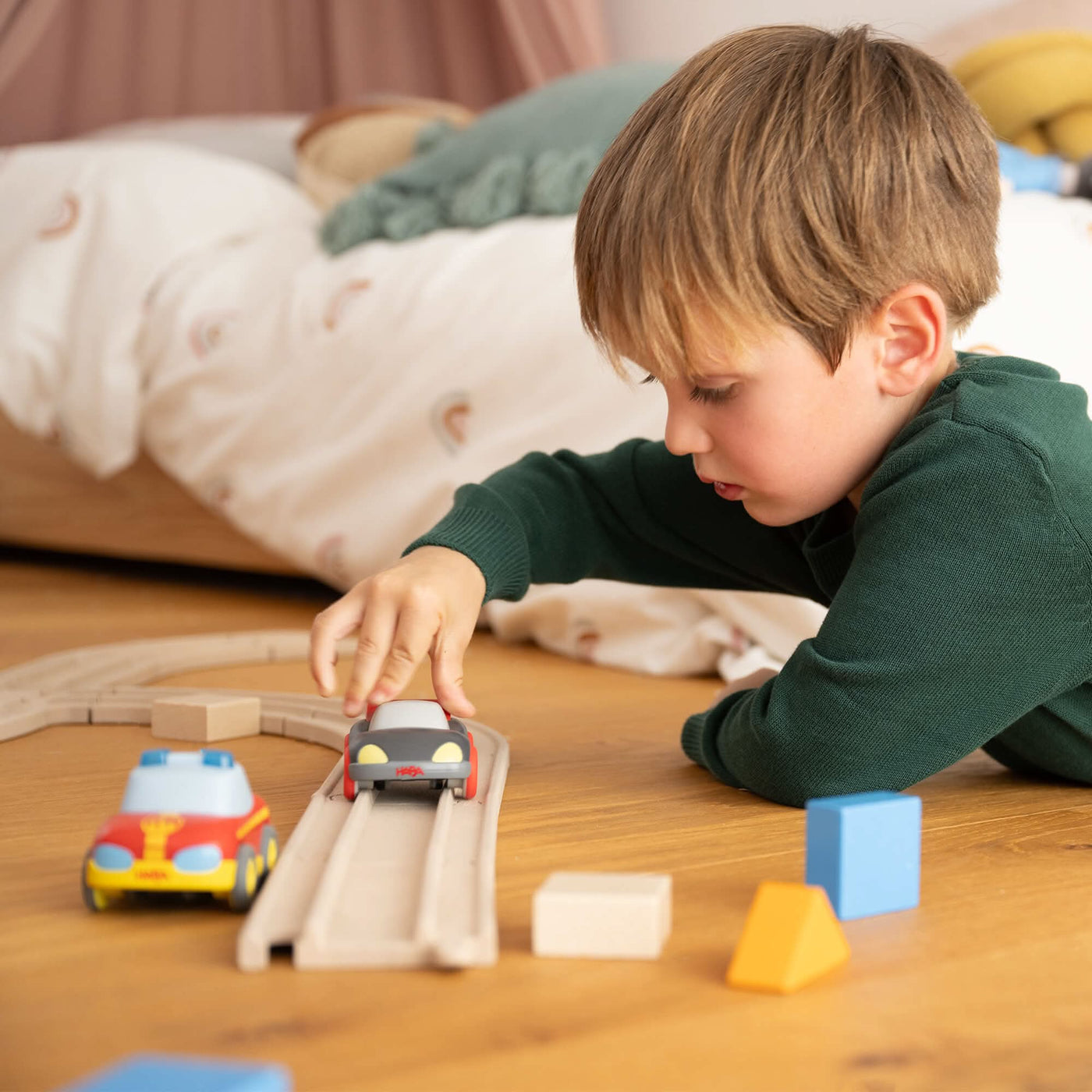 Child playing with toy cars on a wooden track, surrounded by colorful blocks.