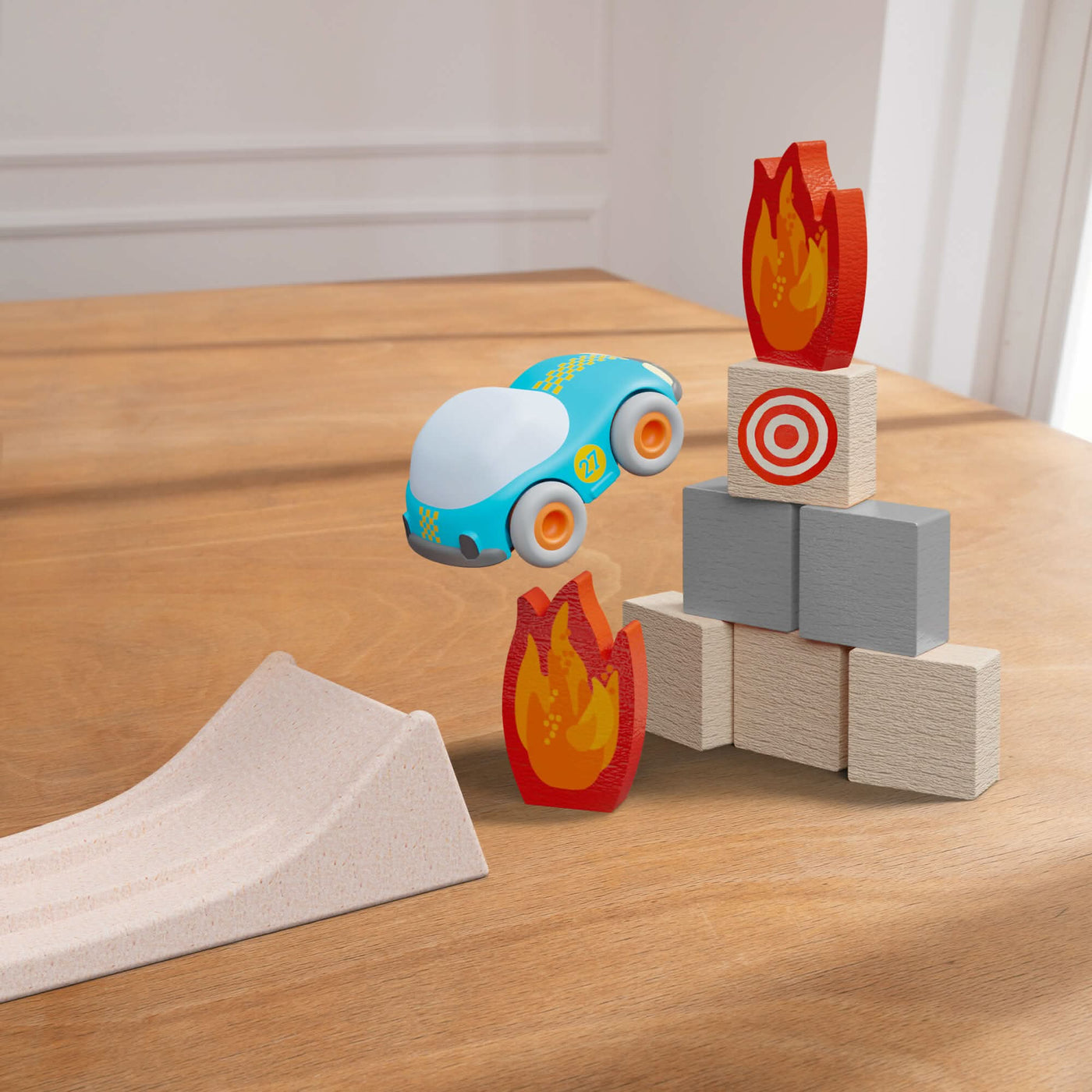 Toy car in mid-air over a wooden table, with a ramp and block tower with flame shapes.