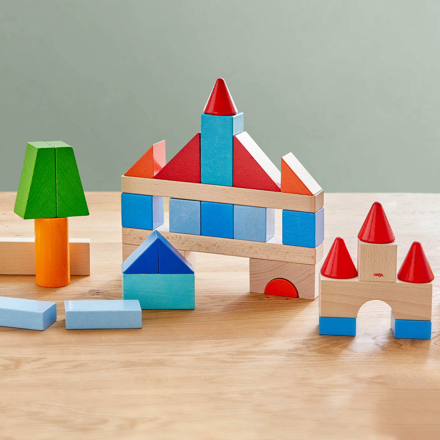 A colorful arrangement of wooden building blocks includes two castles, a tree, and various geometric shapes on a wooden surface.