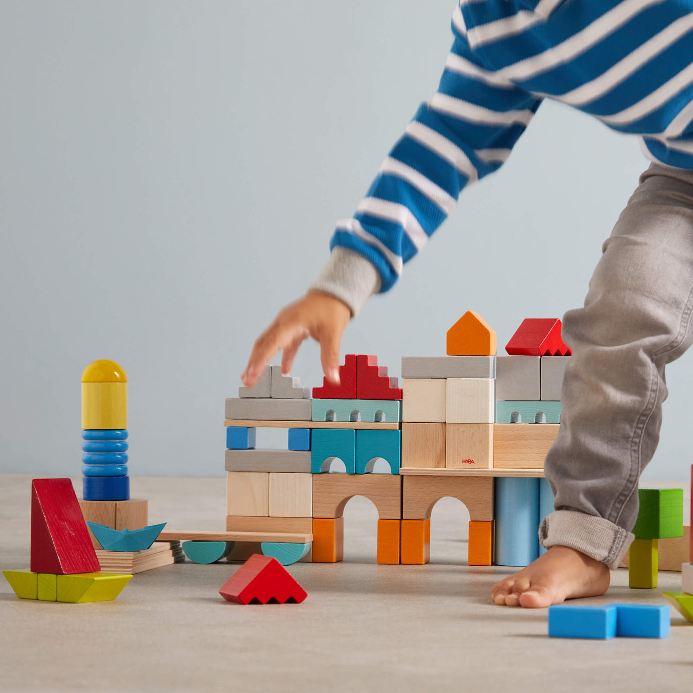 A child in a striped shirt plays with colorful wooden blocks, building a vibrant structure on a light floor.