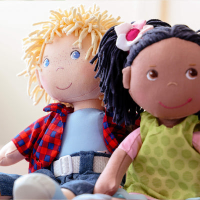 Two fabric dolls sitting together, one with short blonde hair and one with black pigtails