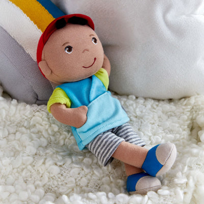 Snug Up Gabriel plush doll on a white textured blanket with a striped cushion behind it.