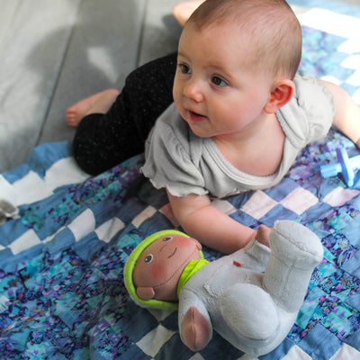 Baby on her tummy on a quilt with HABA Snug Up Doll Ollie