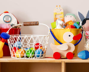 A shelf with a variety of colorful children's toys, including a basket of wooden eggs, a wooden duck on wheels, and a yellow bucket with more toys.