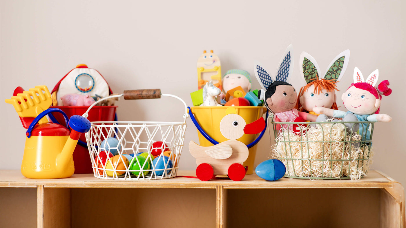 A wooden shelf with colorful children's toys, including a yellow watering can, a wire basket with wooden eggs, a wooden duck toy, and plush dolls.