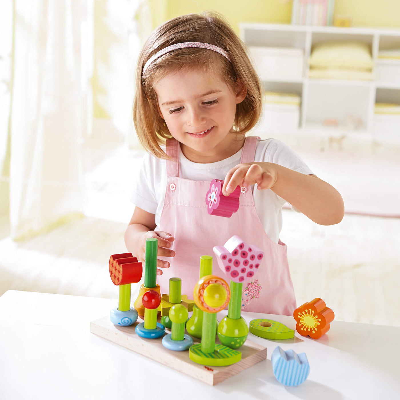 Child building a wooden flower using a pink daisy shape on a green cylinder on a peg board