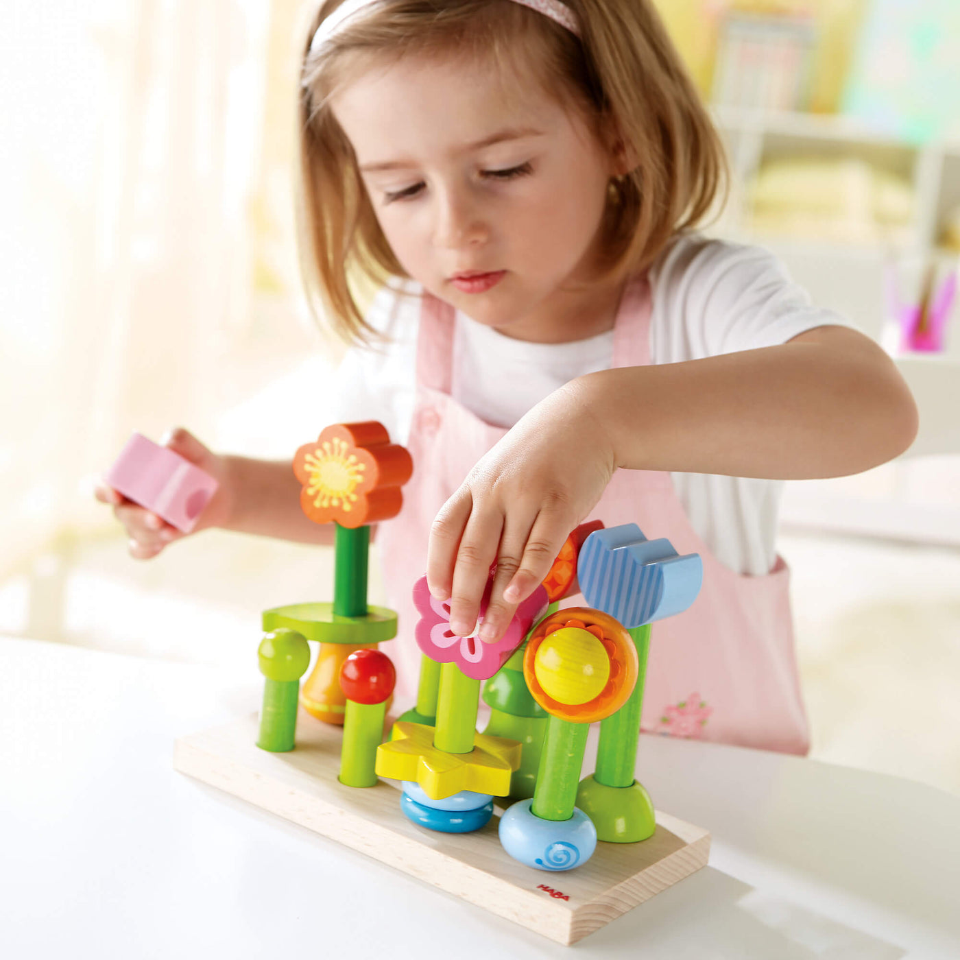 Child building a wooden flower using a pink daisy shape on a green cylinder on a peg board