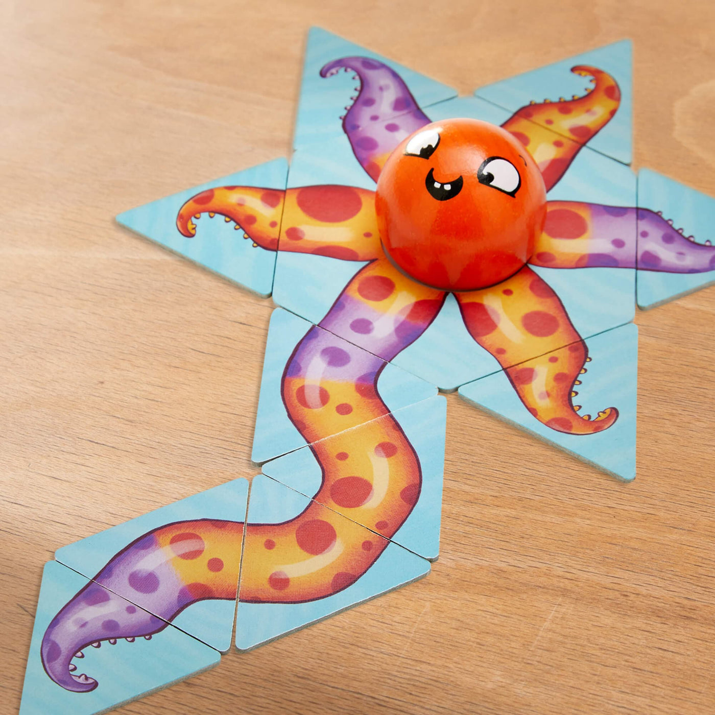 Closeup of orange wooden ball with painted face on blue card tiles with orange and purple tenticle pieces