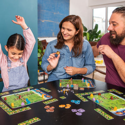 A girl celebrates while playing Karuba board game with her mother and father, all engaged and smiling at the game.