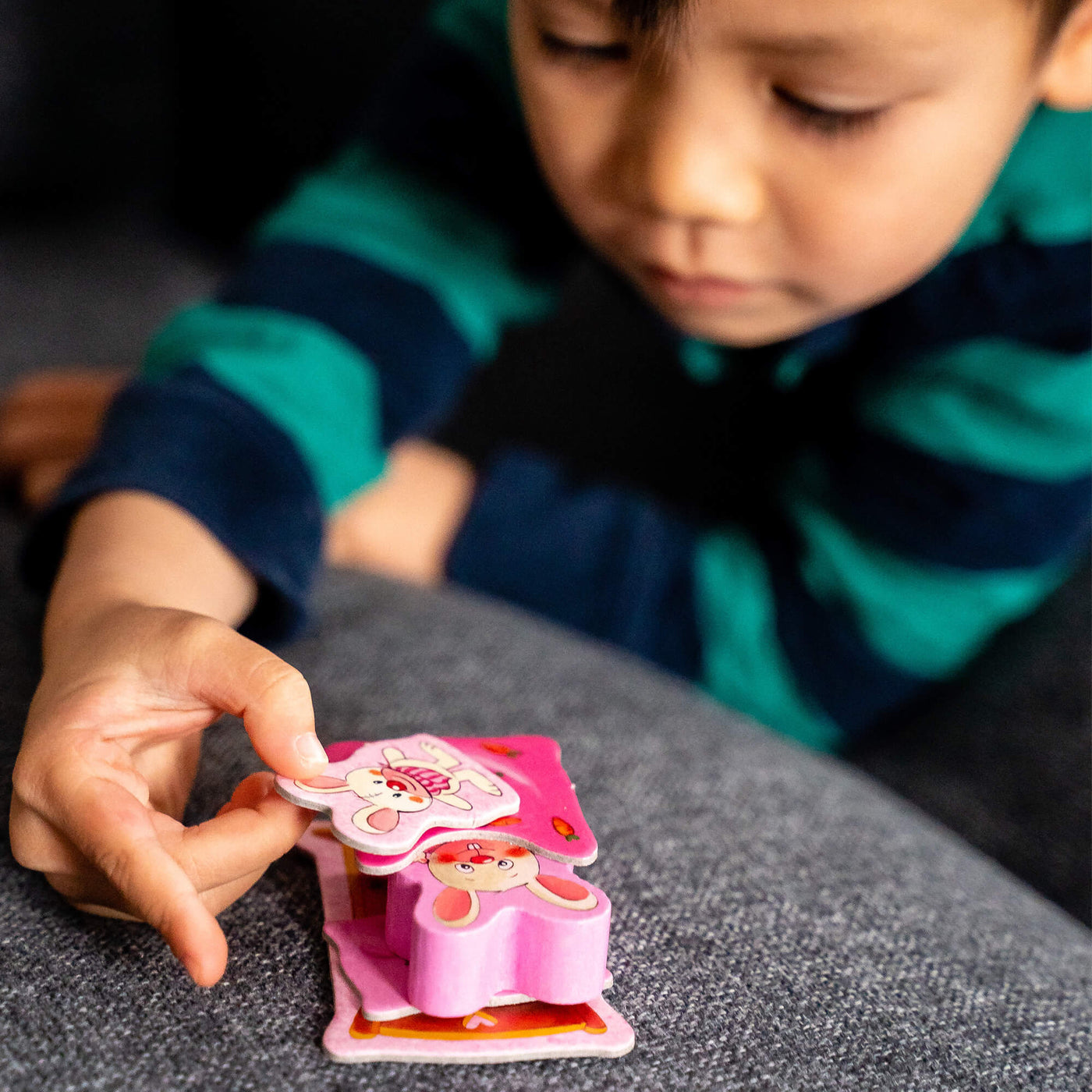 A focused child in a striped shirt places a plush bunny card on a stack with a blanket card and bunny game piece.