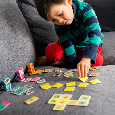 A young child in a striped shirt plays My Very First Games - Off To Bed! with colorful card games on a gray couch, focused on arranging tiles.