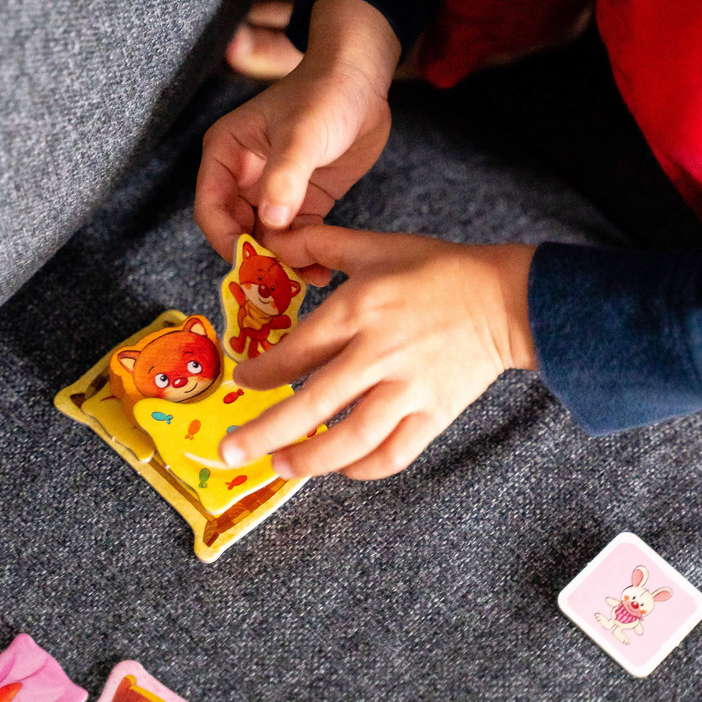 A child’s hands stack a cat plush card on a blanket card on top of the cat piece playing the game Off To Bed!