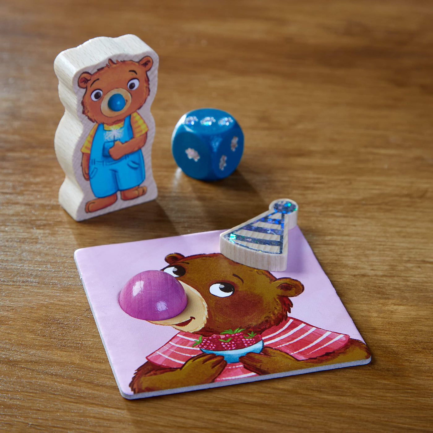 Closeup of wooden bear figure with blue die and purple bear card with wooden party hat and purple wooden nose