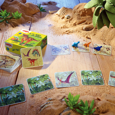 On the Hunt for Dinos game on wooden floor with sand - cards laying on the floor with 2 blue wooden pieces and 1 orange wooden piece