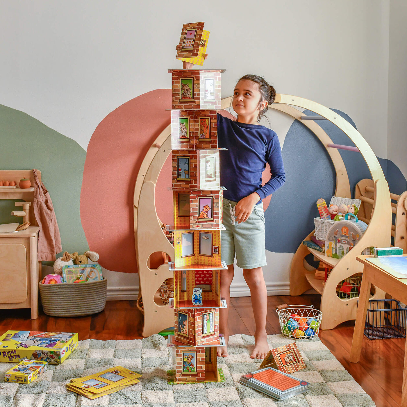 Child standing in a colorful playroom carefully placing a card on top of card tower