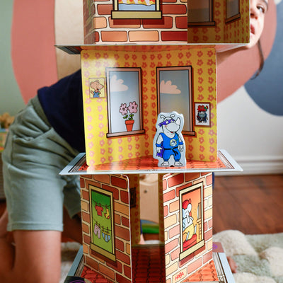 Close up of a card tower with a wooden Rhino Hero game piece set on one of the cards and a child peeking around from the back