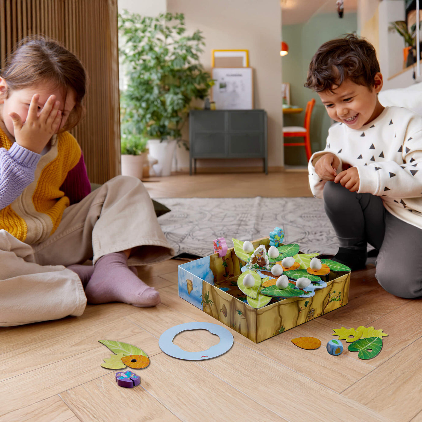 Two children playing a nature-themed board game on a wooden floor.