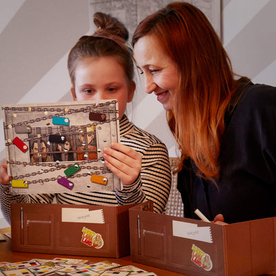 A woman and child play The Key tabletop game peering at a game card depicting characters behind bars