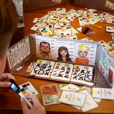 Child looking at The Key game screen with a lineup of three character illustrations in front of a height chart and various cards, with some showing images and text, marked with red X's and circular scribbles underneath.