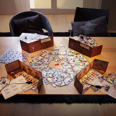 The Key tabletop game with colorful patterned cards, four player screens, and dry-erase markers set up on a wooden table.