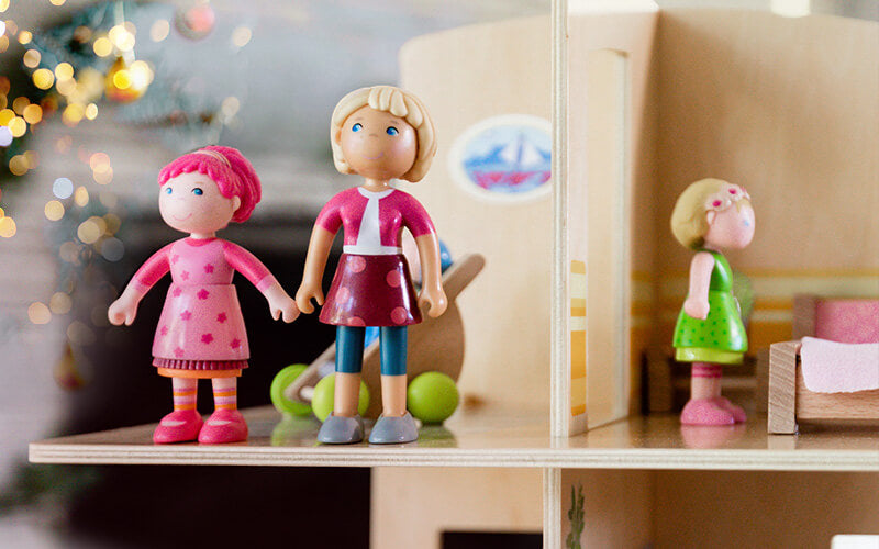 Close up of 3 small Little Friends dolls in a dollhouse with a twinkle lights in the background