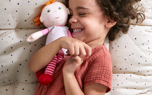 A child smiling while hugging a red-haired Roya doll on a speckled cushion.