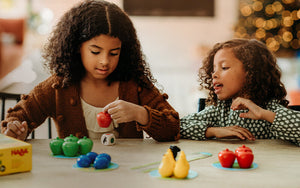 Two girls in front of a Christmas tree playing the HABA game First Orchard