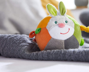 Colorful plush toy shaped like a ball with bunny ears and face on a gray blanket.