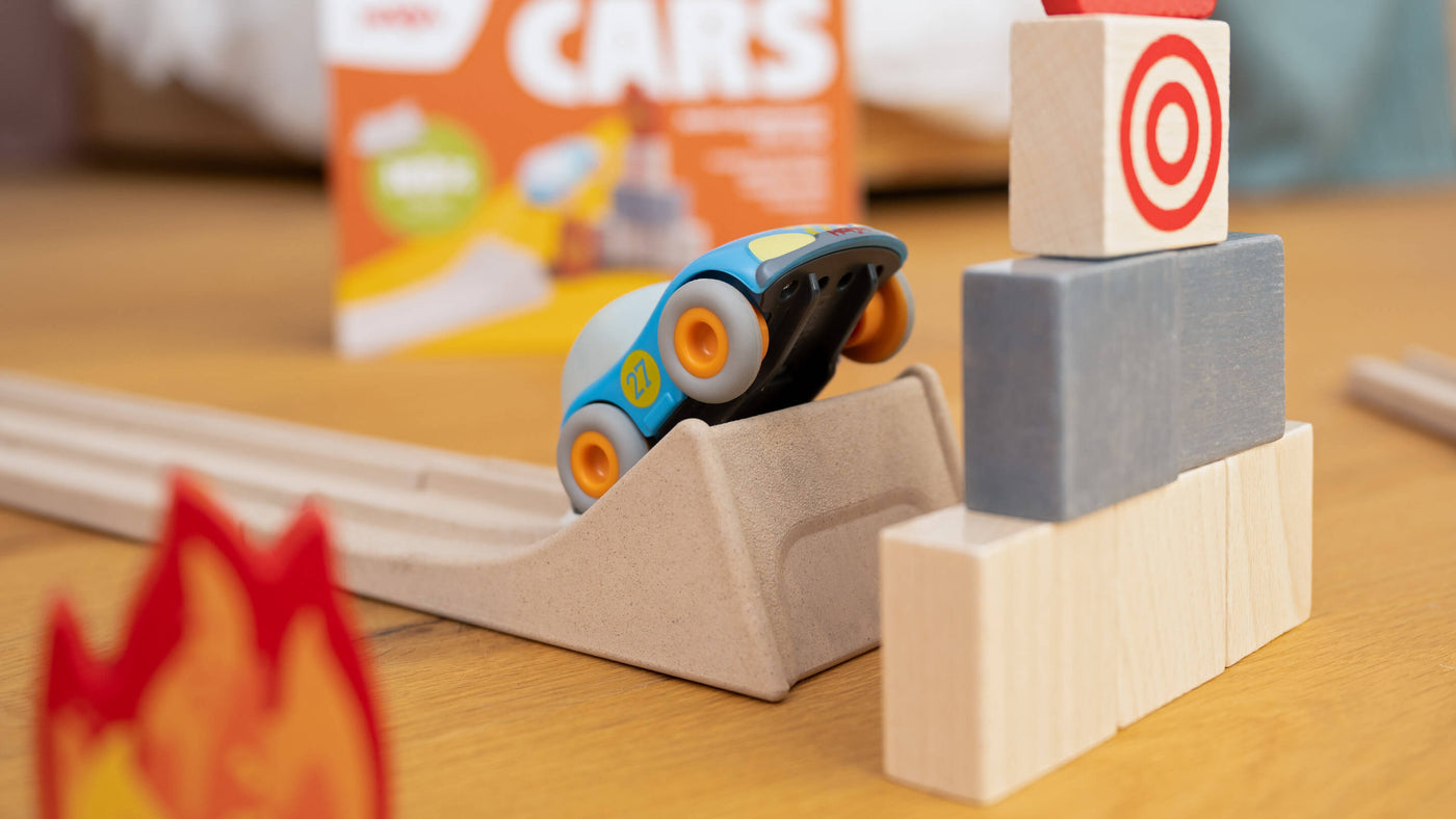 A toy car on a ramp with wooden block tower and a blurred backdrop.