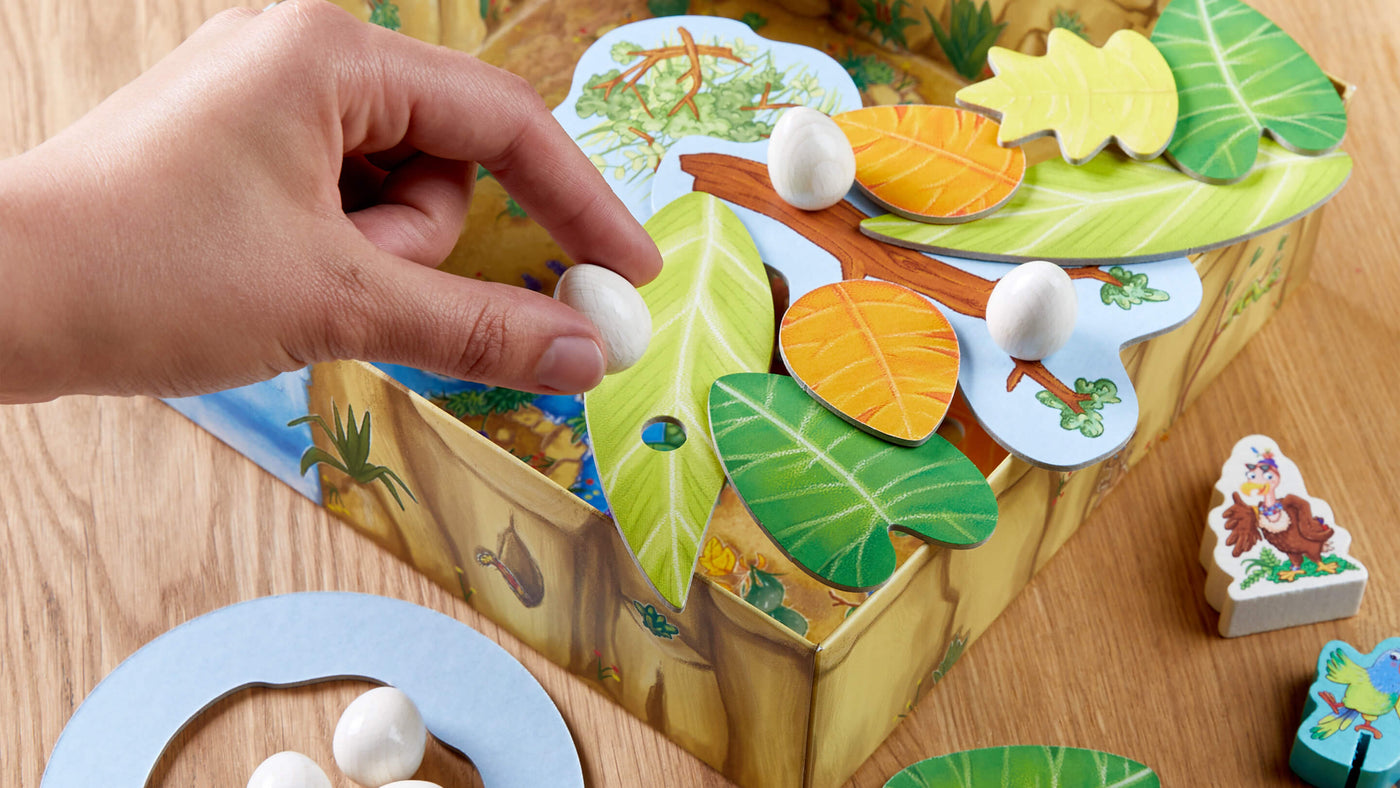 A hand placing a white egg piece onto a board game with colorful leaf-shaped pieces.