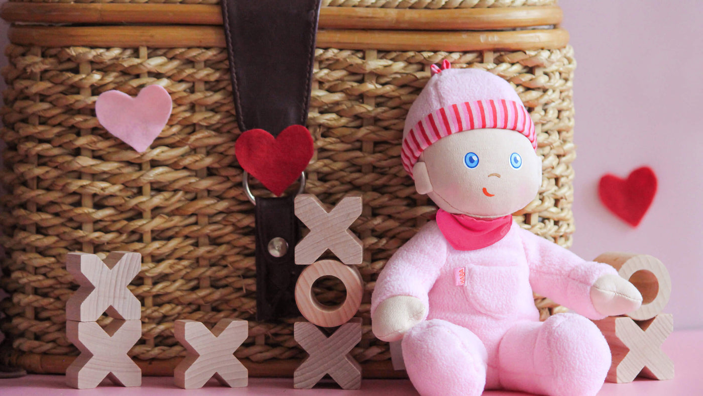 HABA's Luisa doll sitting next to a wicker basket with wooden Xs and Os surrounding