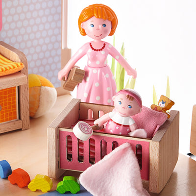 Wooden toy scene with a baby figurine in a crib, and a female figure in a pink polka dot dress nearby.