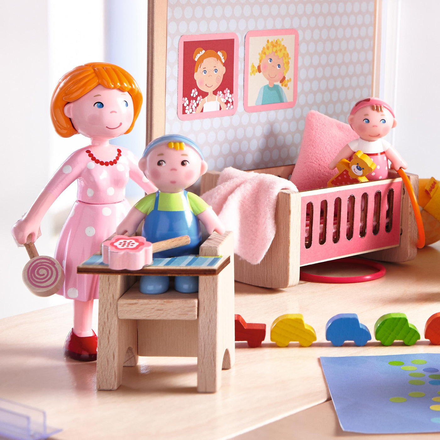 Toy figures depicting a family scene with a woman, a child in a high chair, a crib with another child, and colorful toys.