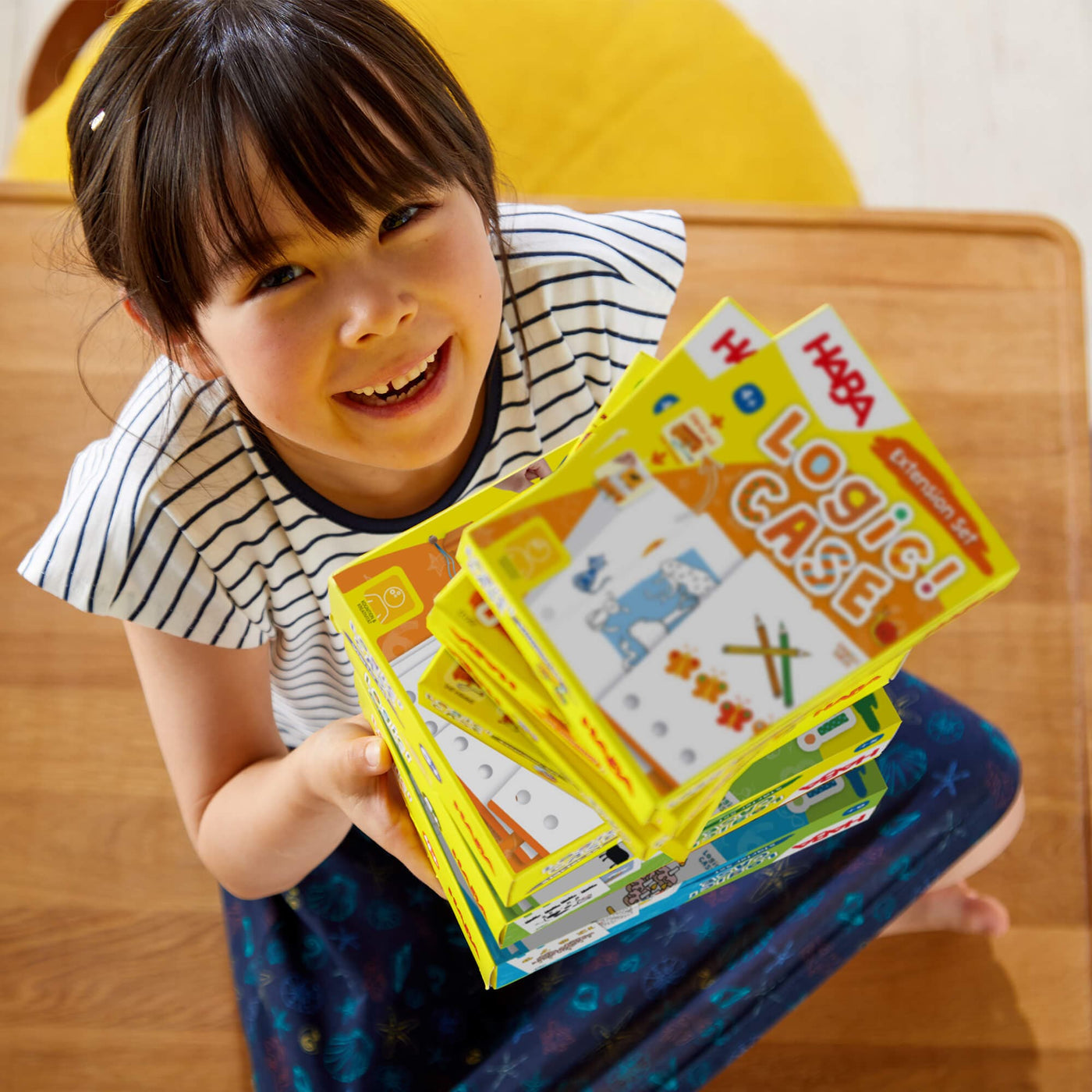 Girl sitting and holding a stack of HABA Logic! CASE puzzle boxes