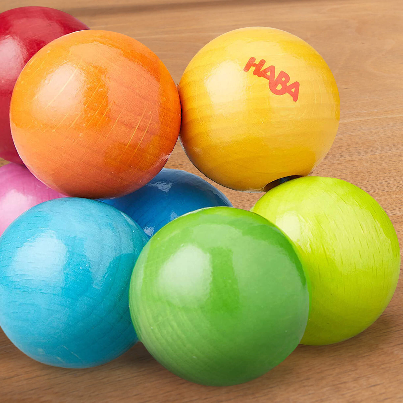 Close up of Magica Wooden Clutching Toy made of of wooden balls in various shades of pink, orange, yellow, blue, green, and red on a light wooden surface.