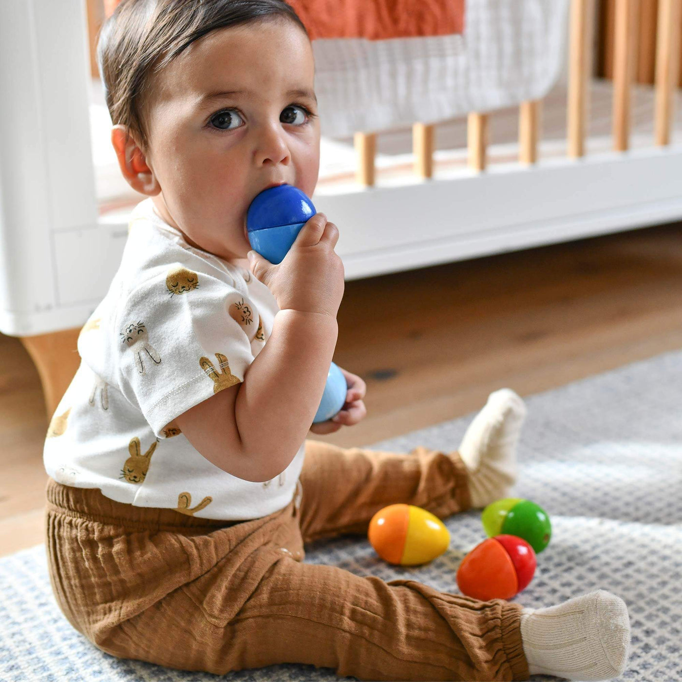 A young boy putting a medium blue Musical Egg in his mouth, sitting on the floor