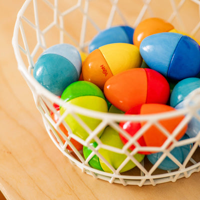 A white basket filled with colorful, wooden egg-shaped toys, featuring vibrant halves of different colors.